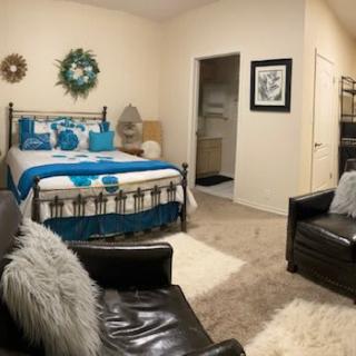 A cozy and modern bedroom with stylish decor, featuring a bed with blue and white bedding, leather armchairs, and a soft rug.