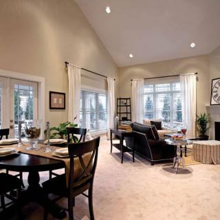 A spacious living room with a connected dining area, featuring large windows and elegant furniture.