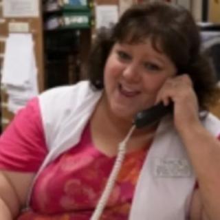 A woman smiling while talking on the phone in an office setting.