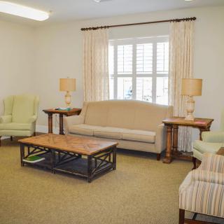 A cozy living room with a sofa, armchairs, and a coffee table, decorated with lamps and curtains.