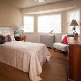 A cozy bedroom with a single bed, wooden furniture, and large windows letting in natural light.