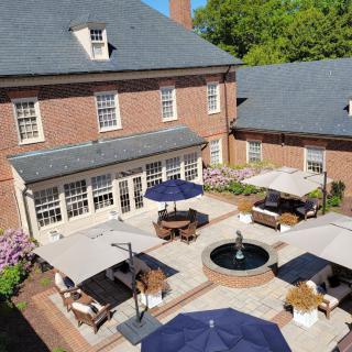 A sunny courtyard with a central fountain surrounded by patio furniture and umbrellas adjacent to a brick building.