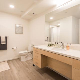 A modern, minimalist bathroom with a large mirror and wooden flooring.