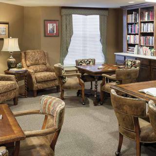A cozy living room with comfortable chairs, wooden tables, and a well-stocked bookshelf.