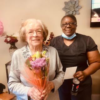 A heartwarming moment between a caregiver and an elderly resident, celebrating with flowers.
