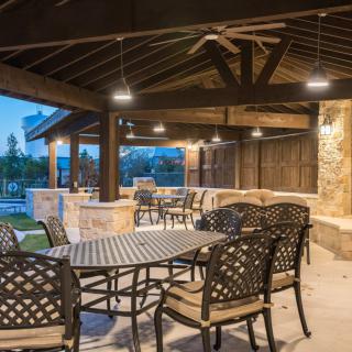 A beautifully designed outdoor patio with dining furniture under a covered structure, illuminated in the evening.