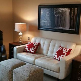 A cozy living room with a white sofa, red and white patterned pillows, warm lighting, and wall art.