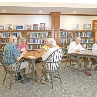 A group of seniors sitting at tables in a library setting, surrounded by bookshelves.