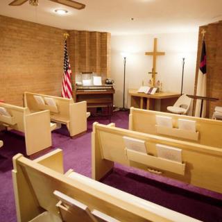 A small chapel with pews, a cross, an American flag, and an organ.