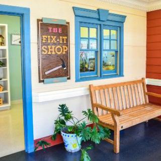 A cozy entrance to a fix-it shop with a wooden bench and potted plants.