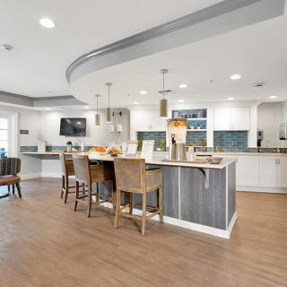 A modern kitchen with an island and bar stools, featuring wood flooring and pendant lighting.