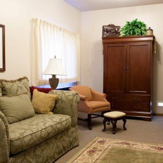 A cozy living room with a sofa, armchair, and large wooden cabinet.