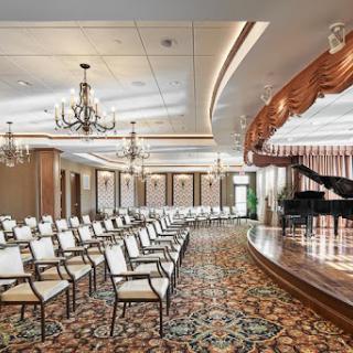 A sophisticated auditorium featuring an elegant stage with a piano and rows of chairs, perfect for performances or events.