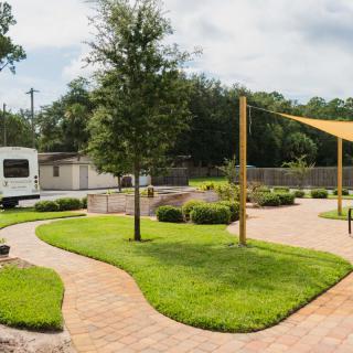 A landscaped garden with a paved walkway, green grass, and a shade sail providing cover.