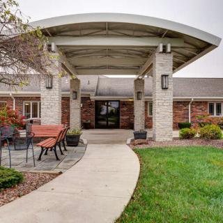 A building entrance with a canopy, featuring a patio area and landscaped greenery.