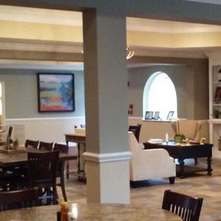 A spacious dining area with tables and chairs, featuring artwork on the walls and natural light from large windows.