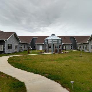 A modern building complex surrounded by grassy areas and pathways under a cloudy sky.