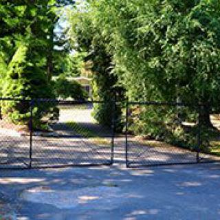 A driveway secured by a metal gate surrounded by lush greenery.