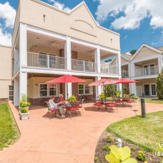 A sunny day at a building with a spacious patio, featuring red umbrellas and outdoor furniture.