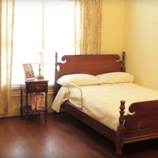 A cozy bedroom with a wooden bed and side table, illuminated by natural light from the window.