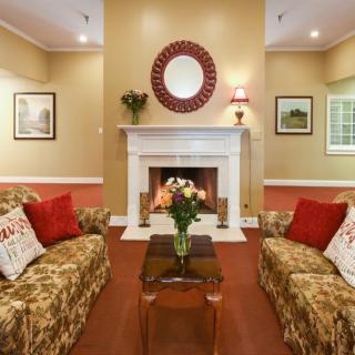 A cozy living room with a central fireplace, featuring two patterned sofas and a decorative mirror above the mantelpiece.