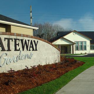 An entrance sign for Gateway Gardens with landscaped surroundings and adjacent buildings.