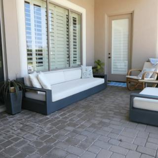 A modern patio with gray outdoor furniture, including a sofa and chairs, set on paver flooring next to large windows.