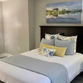 A neatly arranged bedroom with a bed adorned with decorative pillows and a landscape painting on the wall.