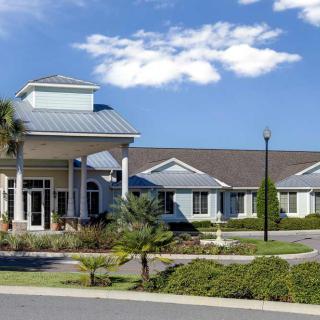 A large building with landscaped surroundings under a blue sky with clouds.