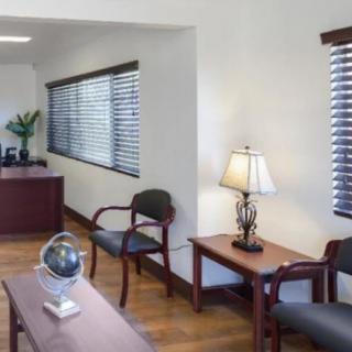 An office waiting area with chairs, a desk, a lamp, and window blinds.
