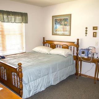 A cozy bedroom with a wooden bed, nightstand, and window with blinds.