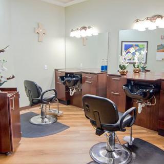A well-lit and spacious hair salon interior featuring styling chairs, mirrors, and sinks on a wooden floor.