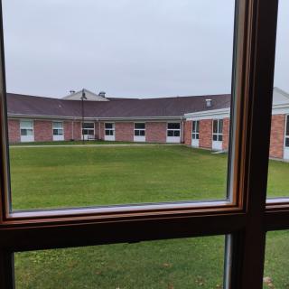 View through a window overlooking a grassy courtyard surrounded by a brick building.