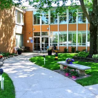A modern building with large windows surrounded by a well-maintained garden and a concrete pathway.