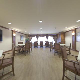 A spacious and elegant dining room with wooden floors, arranged with tables and chairs under soft ceiling lighting.