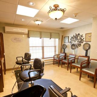 A cozy salon interior featuring styling chairs, mirrors, hair dryers, and a waiting area with comfortable seating.