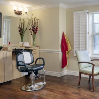 A cozy salon interior with a barber chair, mirror, and decorative flowers by the window.