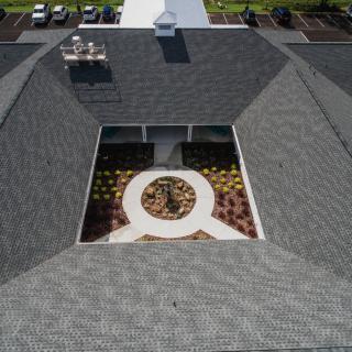 Aerial view of a building with a central courtyard surrounded by a gray shingled roof.