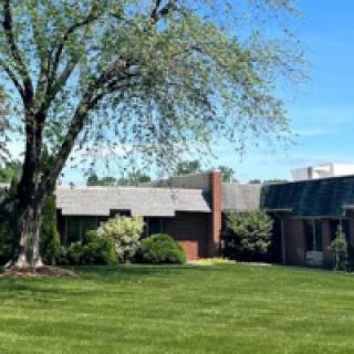 A brick house with a sprawling lawn and a large tree under a clear blue sky.