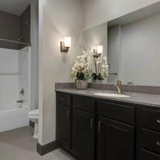 A modern bathroom with dark cabinets, a large mirror, and floral decor.