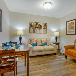 A cozy living room with a beige sofa, orange armchair, wooden dining table, and warm lighting.