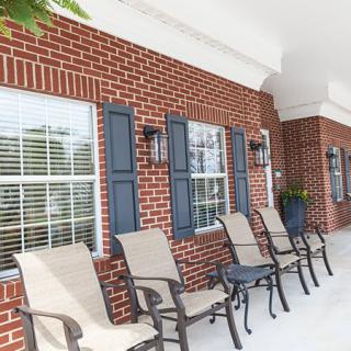 A brick porch with lined-up chairs and windows.