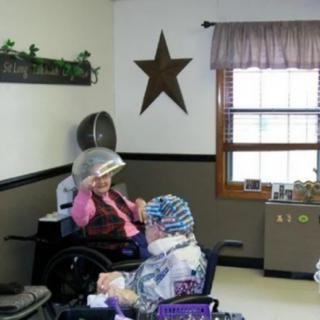 Elderly individuals in a salon setting, seated under hair dryers.