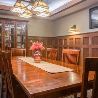 A warmly lit dining room featuring a wooden table with chairs, highlighted by a floral centerpiece and elegant lighting.