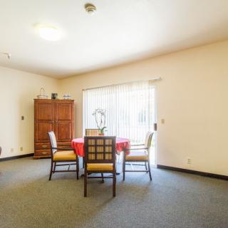 A dining room with a table and four chairs, featuring a large window and a wooden cabinet.