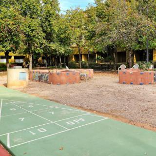 An outdoor playground with a hopscotch court, surrounded by trees and seating areas in a park.