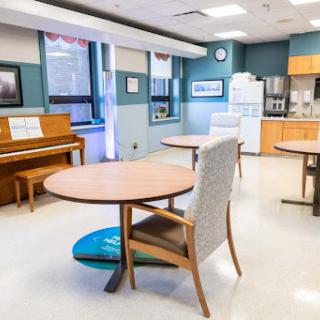 A spacious and inviting common area featuring tables, chairs, a piano, and a kitchenette.