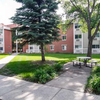 A peaceful outdoor area with benches and trees in front of an apartment building.