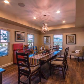 A cozy, traditional-style dining room with a chandelier and wooden flooring, illuminated by natural light from the surrounding windows.