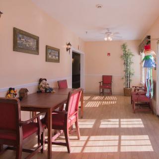 A sunlit dining room with a wooden table and red chairs, featuring wall decor and a potted plant.